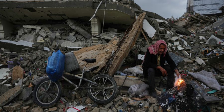 dpatopbilder - Der Palästinenser Mohammed al-Jabri, 58, wärmt sich neben dem Feuer, während er auf den Trümmern eines Gebäudes sitzt, das während der israelischen Luft- und Bodeno...