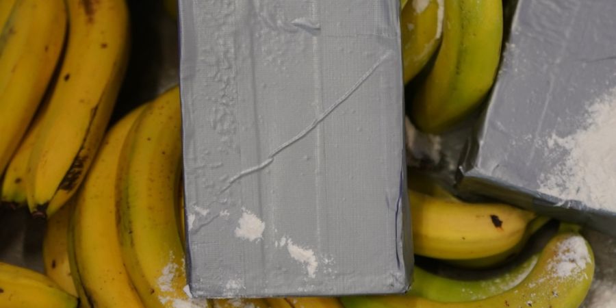 ILLUSTRATION - Silber-graue Pakete und weißes Pulver, das Kokain darstellen soll, liegt neben Bananen und Bananenkisten während der Vorstellung einer Awareness-Kampagne für Hafenbesc...
