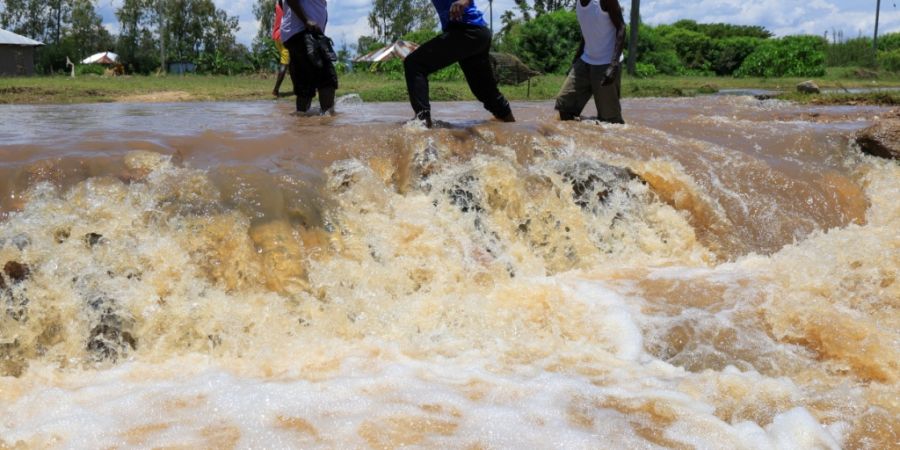 Menschen überqueren einen überfluteten Straßenabschnitt nach schweren Regenfällen in Kenia. Foto: Andrew Kasuku/AP/dpa
