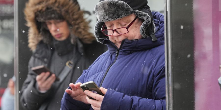 ARCHIV - Menschen schauen auf ihre Smartphones an einer Bushaltestelle in St. Petersburg. Foto: Dmitri Lovetsky/AP/dpa/Archivbild