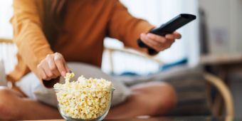 Frauenhand nimmt Popcorn und hält Fernbedienung