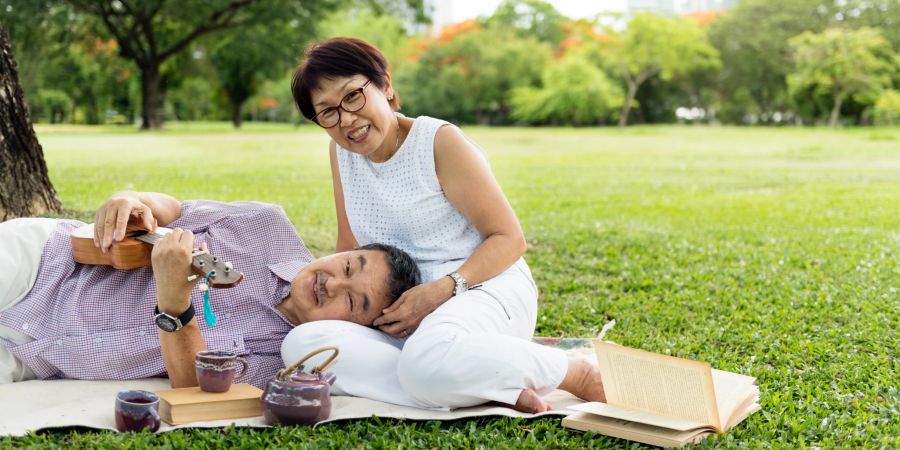 asiatisches paar im park, er spielt ukulele, sie lächelt