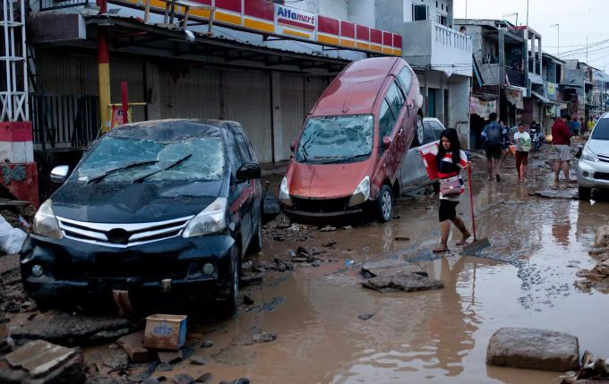 Ein Mädchen geht auf einer überschwemmten Strasse an zerstörten Autos vorbei. Überschwemmungen in Indonesien