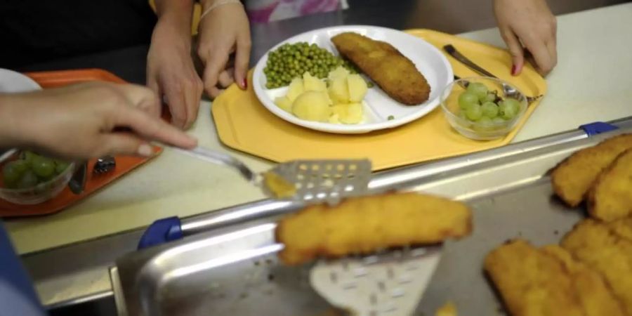 Eine Küchenhelferin legt an einer Gesamtschule ein Stück Fisch auf den Teller eines Schülers. Foto: Alexander Körner/dpa