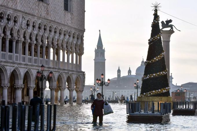 Eine Frau watet über den überfluteten Markusplatz. Hochwasser in Venedig