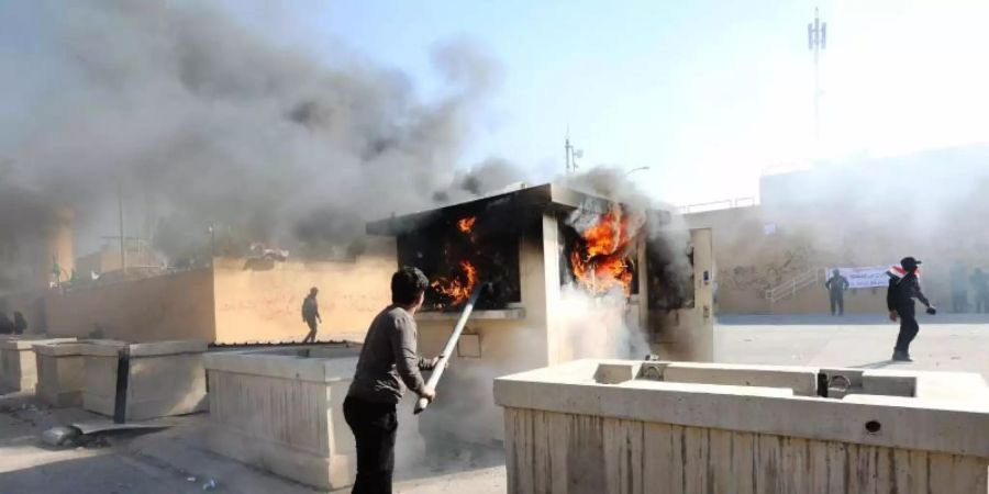 Ein Demonstrant schürt vor der Botschaft der Vereinigten Staaten in Bagdad ein Feuer. Foto: Khalil Dawood/XinHua/dpa