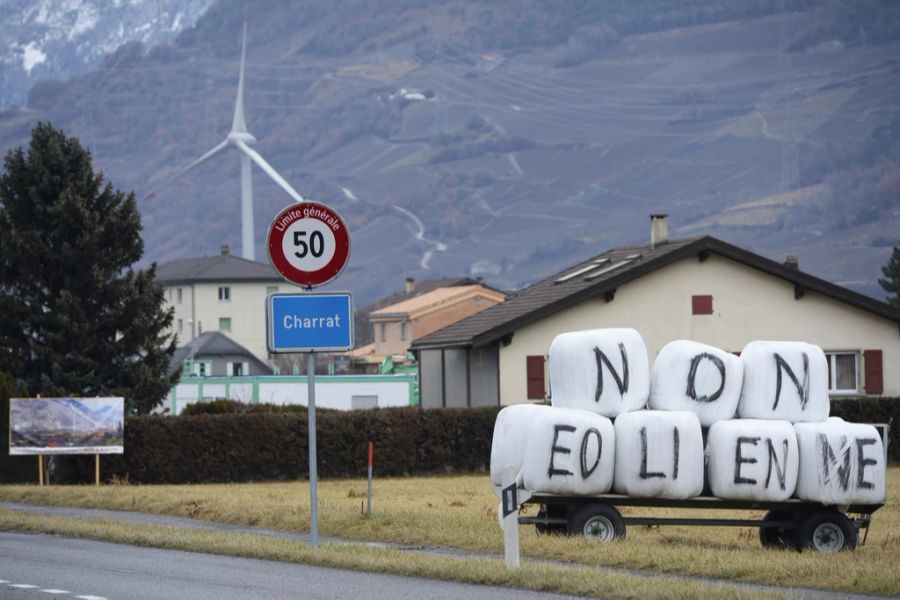 Ein Anhänger mit Heuballen und der Aufschrift «NON EOLIENNE» («Nein Windräder») steht am Dorfeingang von Charrat VS, mit der Windturbine im Hintergrund.