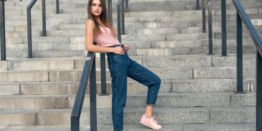 Junge Frau posiert in Jeans und rosa Top auf einer Steintreppe.