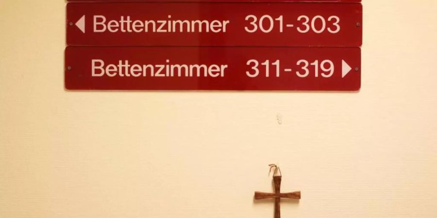 Ein kleines Holzkreuz hängt unter Hinweisschildern auf einer Station in einem kirchlichen Krankenhaus. Foto: Christian Charisius