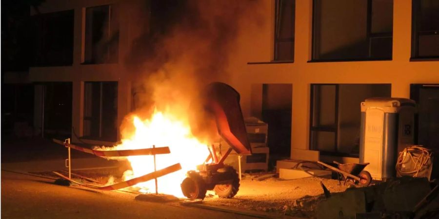 Eine Baumaschine, welche neben einem Mehrfamilienhaus abgestellt wurde, brennt.