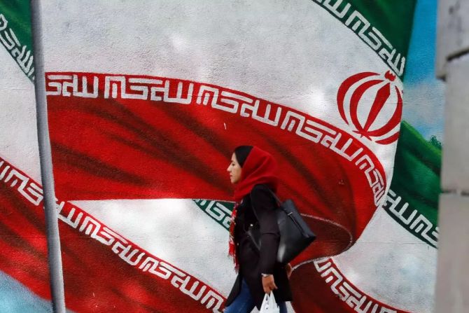 Eine Frau läuft an einer Mauer vorbei, auf der zwei iranische Flaggen abgebildet sind.