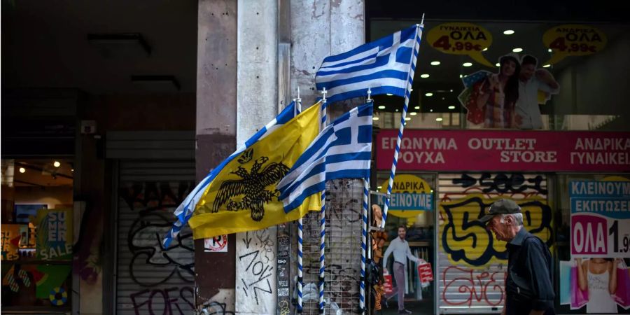 Ein Mann geht im Stadtzentrum an griechischen Flaggen vorbei.