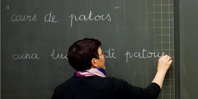 Eine Lehrerin unterrichtet Patois und schreibt damit mit Kreide auf die Wandtafel. Eine Lehrerin unterrichtet Patois und schreibt damit mit Kreide auf die Wandtafel.