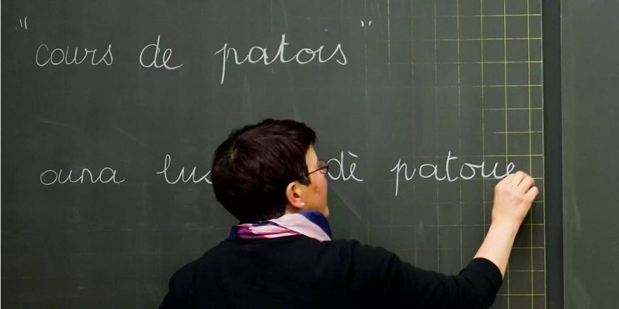 Eine Lehrerin unterrichtet Patois und schreibt damit mit Kreide auf die Wandtafel.