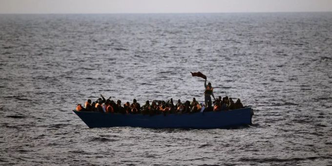 Mittelmeer-Flüchtlinge winken auf einem Holzboot um Hilfe. Flüchtlinge winken auf einem Holzboot um Hilfe.