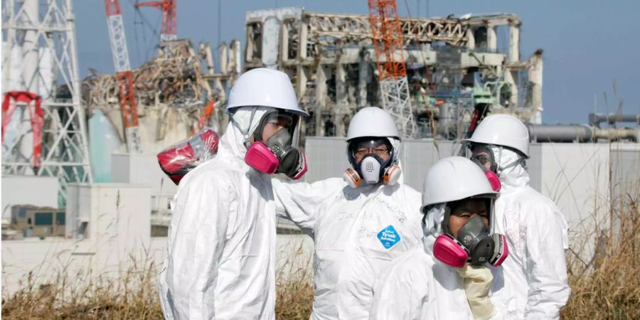 Medienmitarbeiter und Helfer in Schutzanzügen vor dem zerstörten Reaktor von Fukushima Daiichi im März 2011.