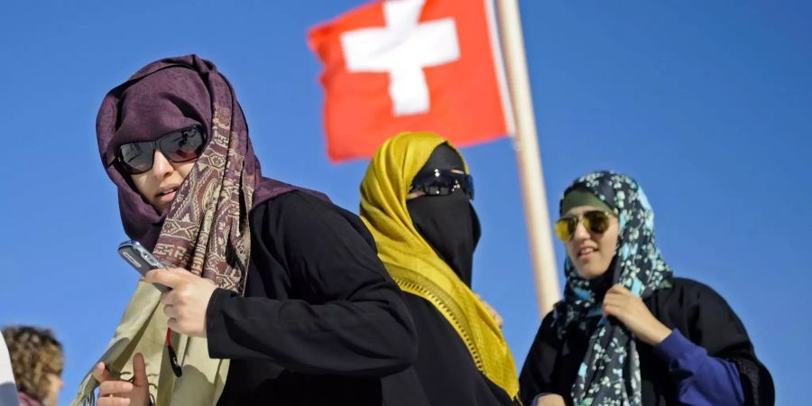 Touristinnen mit Kopftuch vor einer Schweizer Nationalflagge auf dem Jungfraujoch im Berner Oberland.