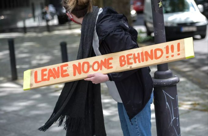 Eine Teilnehmerin einer Protest-Aktion hält ein Schild mit der Aufschrift «Leave No-One Behind». Corona-Demo