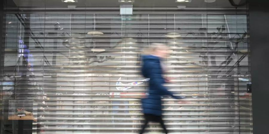 Eine Frau geht auf der Frankfurter Einkaufsmeile Zeil an einem Geschäft vorbei, an dem noch das Rollgitter heruntergelassen ist. Durch die Corona-Krise droht vielen innerstädtischen Geschäften das Aus. Foto: Arne Dedert/dpa