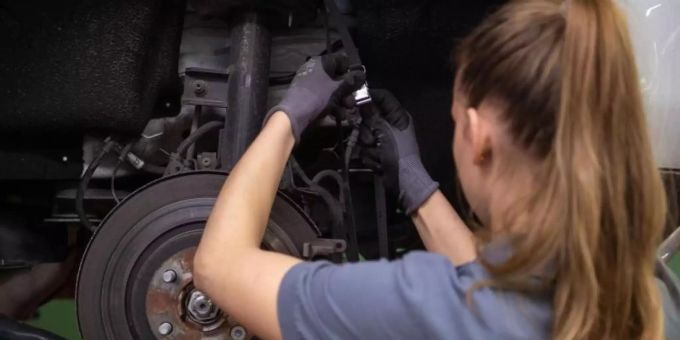 Eine Kfz-Mechanikerin wechselt in einer Werkstatt die Bremsscheibe eines Autos. kfz frau