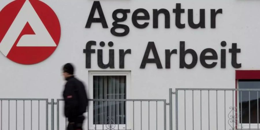 Ein Mann geht an dem Logo der Agentur für Arbeit vorbei. Foto: Sebastian Kahnert/dpa-Zentralbild/dpa