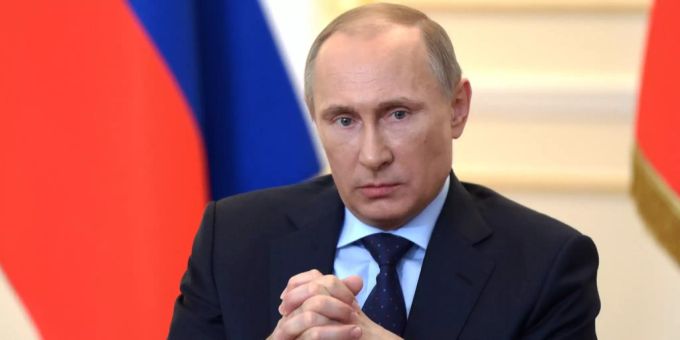 Wladimir Putin sitzt zwischen zwei russischen Flaggen. Wladimir Putin