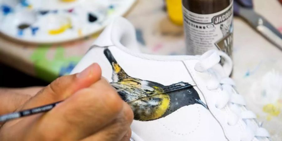 Ein Turnschuh wird in der Manufaktur «Sneaker Surgery» mit einem Bild des neuseeländischen Vogels Hihi (Gelbbandhonigfresser) bemalt. Foto: Daniel Bockwoldt/dpa