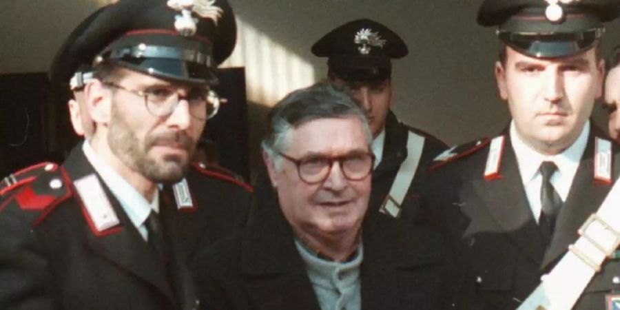 Der italienische Mafiaboss Salvatore Riina (M) wird von Polizisten in Handschellen in den Gerichtssaal geführt. Foto: Gianni Schicchi/AP