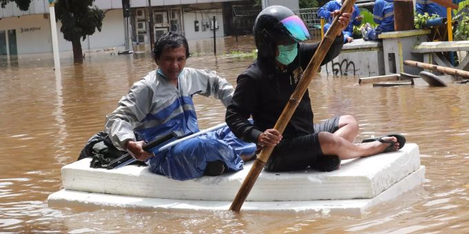 20.02.2021, Indonesien, Jakarta: Anwohner benutzen Schaumstoff als Floss, um sich einen Weg durch eine überflutete Strasse nach starken Regenfällen zu bahnen. Heftige Regenfälle haben in Teilen von Indonesiens Hauptstadt Jakarta zu Überschwemmungen geführt und Hunderte Menschen in die Flucht getrieben. Foto: Tatan Syuflana/AP/dpa +++ dpa-Bildfunk +++ Überschwemmung in Indonesien