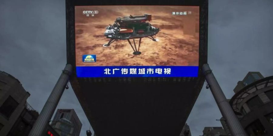 Feiertag für das chinesische Staatsfernsehen: Eine Nachrichtensendung über die erfolgreiche Landung einer Sonde auf dem Mars wird auf einem grossen Videobildschirm gezeigt. Foto: Mark Schiefelbein/AP/dpa