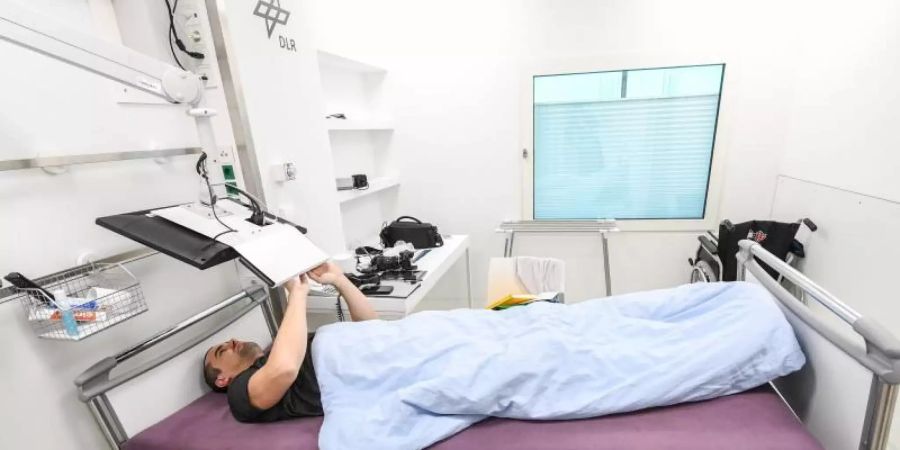 Ein Teilnehmer der Bettruhestudie arbeitet am Computer, während er im Bett liegt. Foto: DLR/dpa