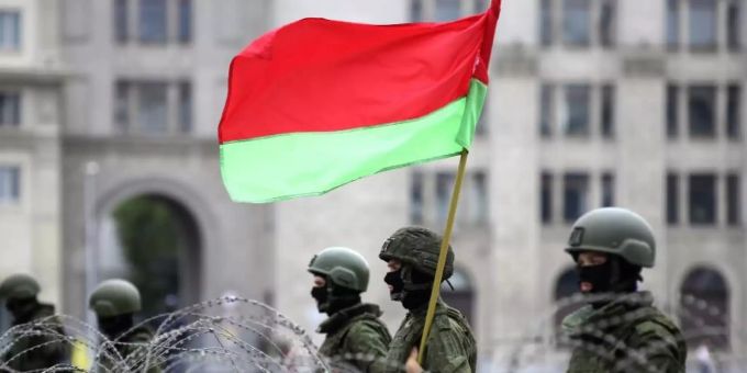 Uniformierte Sicherheitskräfte stehen in Minsk mit der belarussischen Staatsflagge hinter Stacheldraht. Foto: Uncredited/Tut.by/AP/dpa belarus