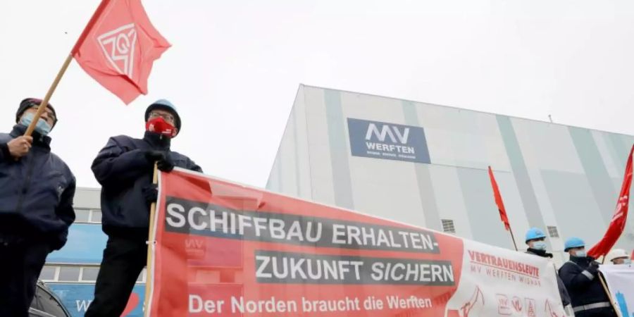 Beschäftigte der Werft stehen mit Fahnen und Transparenten vor der Schiffbauhalle in Wismar. Foto: Bernd Wüstneck/dpa-Zentralbild/dpa