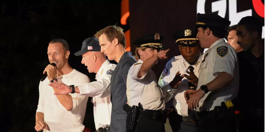 Polizisten besprechen die Lage auf der Bühne des Global Citizen Festivals, während Chris Martin mit dem Publikum sprich