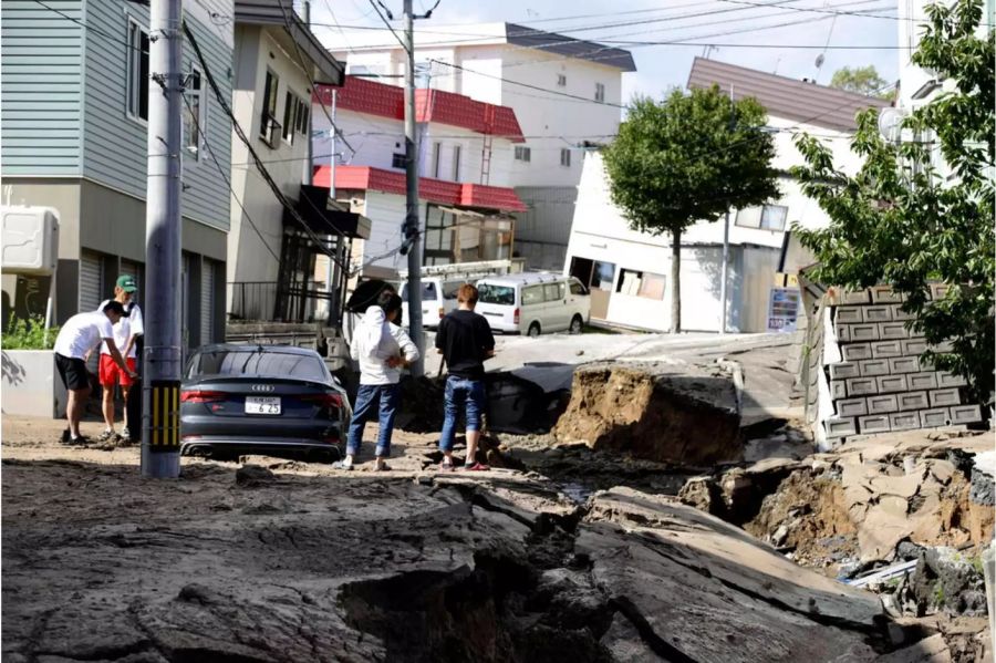 Mehrere Männer begutachten die bei dem Erdbeben auf der japanischen Insel Hokkaido völlig zerstörte Strasse.