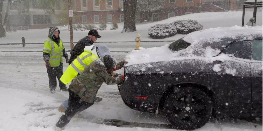 Bei dichtem Schneefall schieben ein Polizist und Passanten ein Auto an.