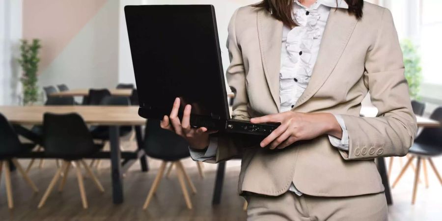 Eine Frau im Business-Look und einem Laptop in der Hand steht in einem Konferenzsaal.