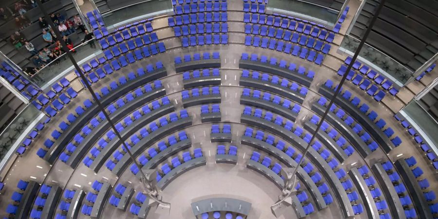 Eine Gruppe Besucher sitzt im leeren Plenarsaal des Reichstages in Berlin.