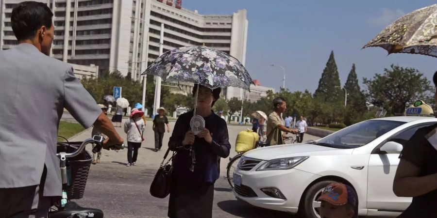 Eine japanische Frau kühlt sich in der sengenden Hitze mit Sonnenschirm und Ventilator ab. (Symbolbild)