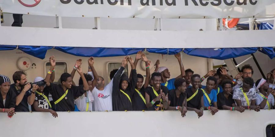 Migranten und Besatzungsmitglieder des Rettungsschiffes Aquarius winken beim Einlaufen in den Hafen von Senglea. Das Schiff mit 141 aus Seenot geretteten Menschen an Bord hatte fünf Tage auf hoher See warten müssen, bevor Malta sich bereit erklärte, es anlanden zu lassen.