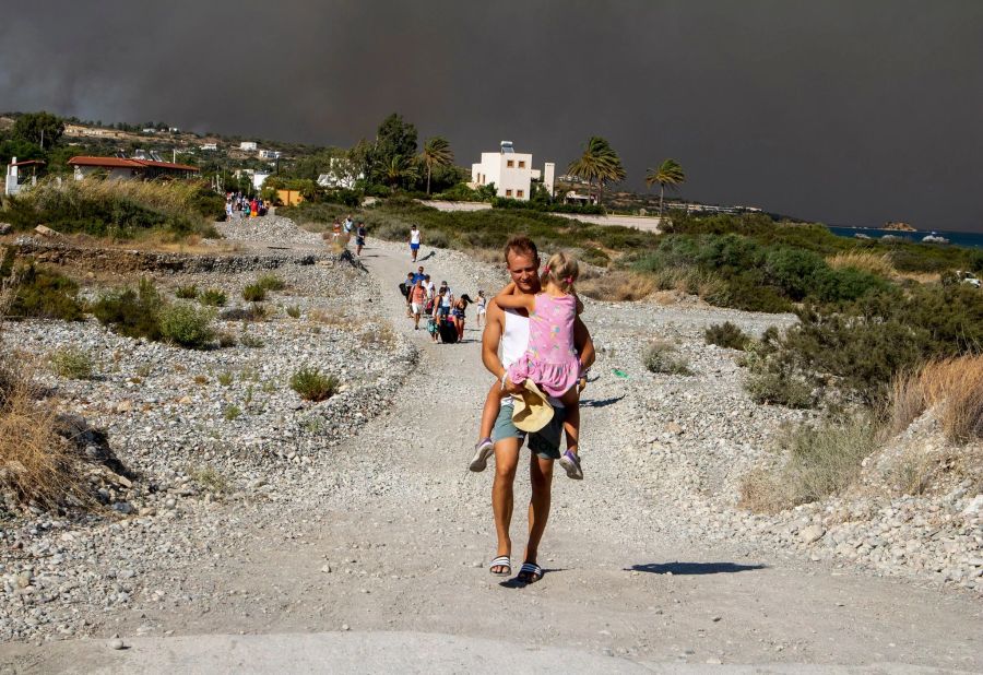 Menschen verlassen ein Waldbrandgebiet auf Rhodos. Auf der griechischen Insel wüten weiter mehrere Brände.