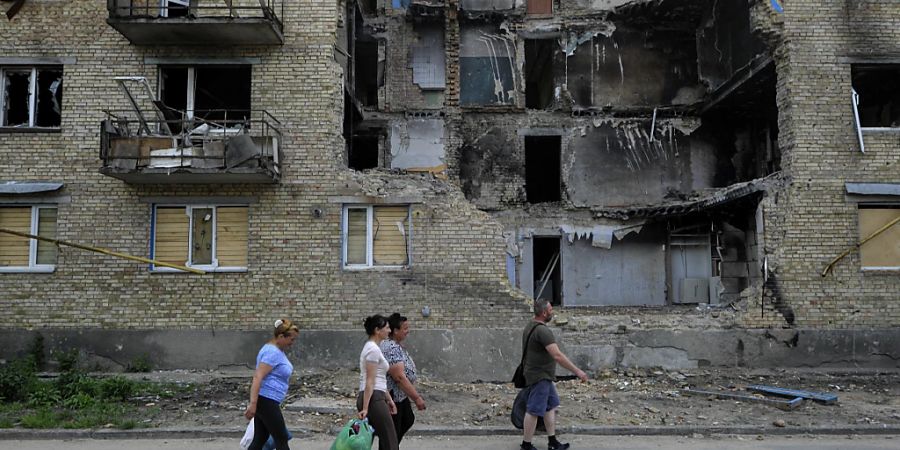 Menschen tragen humanitäre Hilfsgüter an einem zerstörten Wohnhaus vorbei, das durch den Beschuss der russischen Armee beschädigt wurde. Foto: Sergei Chuzavkov/SOPA Images via ZUMA Press Wire/dpa