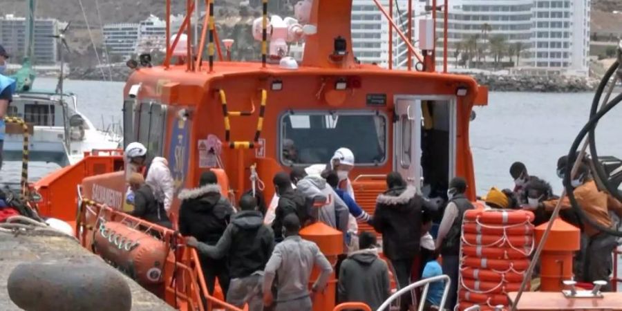 Mitarbeiter in Schutzkleidung der Salvamento Maritimo helfen im Hafen von Arguineguin Migranten an Land. (Archivbild). Foto: Europa Press/dpa
