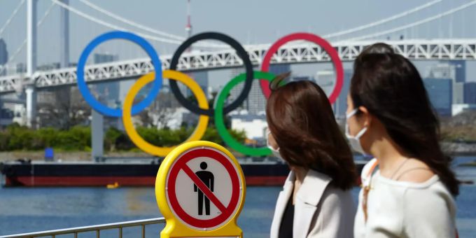 Zwei Frauen gehen an einem «Betreten verboten»-Schild vorbei. Dahinter sind die Olympischen Ringe zu sehen. Foto: Eugene Hoshiko Vor den Olympischen Spielen in Tokio
