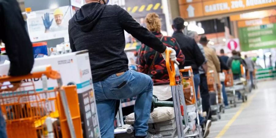 Kunden stehen mit Einkaufswagen in einem Hornbach-Baumarkt in einer Schlange vor den Kassen an. Foto: Sven Hoppe/dpa