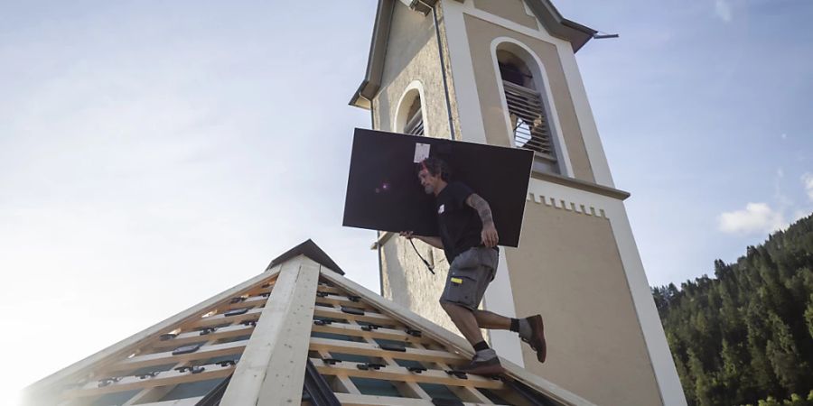 Arbeiter montieren Solarpanels auf dem Dach der historischen reformierten Kirche in Trin, einem Bündner Bergdorf am Rand der Ferienregion Flims-Laax.