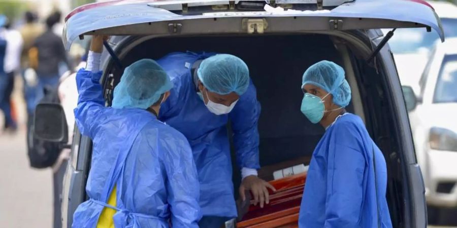 Männer mit Schutzanzügen laden in der Hafenstadt Guayaquil in Ecuador einen Sarg in einen Wagen vor einem Krankenhaus. Foto: Marcos Pin Mendez/dpa