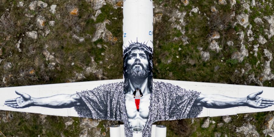 Der Berner Künstler Vierwind alias Micha Haeni in roter Hose auf seinem Kunstwerk: der gekreuzigte Christus, gemalt auf auf ein Flugzeug und betrachtet aus der Himmelsperspektive. Für...