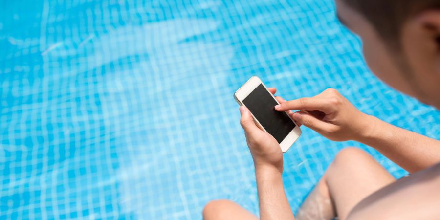 Mann mit Smartphone am Pool