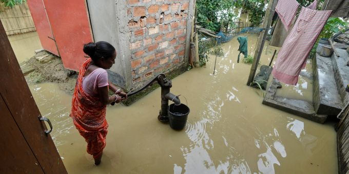 Eine Frau versucht in der überfluteten Umgebung ihres Hauses, Wasser zu sammeln. Überflutung